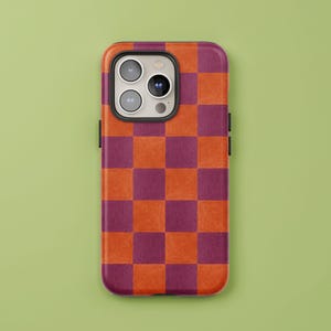 May include: A phone case with a checkerboard pattern in shades of orange and burgundy. The case has a glossy finish and a black camera lens frame. The phone case is shown against a green background.