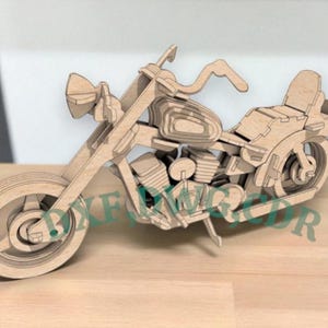 May include: A wooden motorcycle model with intricate details, including wheels, handlebars, and a seat. The model is made of light-colored wood and appears to be a DIY kit or a decorative item. The text "XKE CDR" is visible on the bottom of the image.