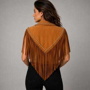 May include: A tan suede vest featuring a V-shaped back yoke adorned with metallic studs. The garment has long, flowing fringe detailing that extends from the shoulders down to a point at the center back, creating a layered appearance.