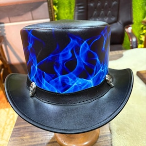 Peut inclure: Haut-de-forme noir avec un motif de flammes bleues. Le chapeau a un large bord et des ornements de crânes argentés sur le bandeau. Il est présenté sur un support à chapeau en bois.