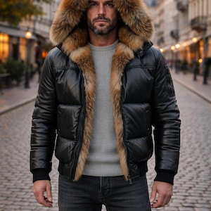 May include: Black leather puffer jacket with a fur-lined hood and trim. The jacket has a bomber style with a ribbed hem and cuffs. The model is wearing a gray sweater and dark wash jeans. The jacket is a stylish outerwear option.