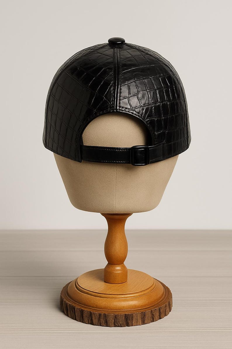 May include: Black baseball cap with a textured, crocodile-like pattern. The cap features a curved brim, a button on top, and an adjustable strap with a buckle. The cap is displayed on a mannequin head.