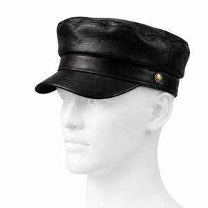 May include: A black leather cap with a short brim and a rounded crown. The cap features a decorative button on the side and a band around the base. The hat is displayed on a white mannequin head.
