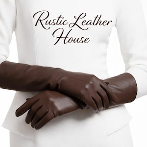 Peut inclure: Longues gants en cuir marron foncé. Les gants sont d'un brun profond et remontent sur le bras. Le texte "Rustic Leather House" est affiché en écriture cursive.