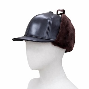 May include: A dark brown leather cap with a short peak and ear flaps. The ear flaps are made of a dark brown, fuzzy material. A brown ribbon is attached to the back of the cap.
