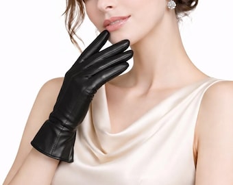 Könnte beinhalten: Ein Paar schwarze Lederhandschuhe mit glatter Oberfläche, sichtbaren Nähten an den Fingern und am Handgelenk sowie einem ausgestellten Manschettendesign. Die Handschuhe haben eine eng anliegende Passform.