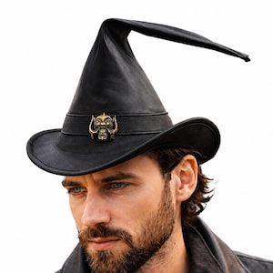 May include: Black leather hat with a unique, elongated, curved brim. The hat features a wide brim and a tall, pointed crown. A decorative gold-colored emblem is affixed to the hatband. The hat is a blend of witch and cowboy hat styles.