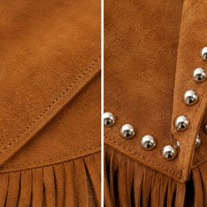 May include: A tan suede garment featuring a layered flap design with visible stitching. The right side displays a row of polished silver-toned metal studs along the edge, and the bottom hem is finished with long, matching tan suede fringe.