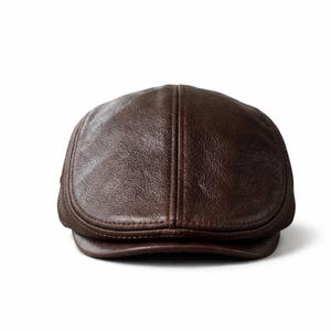 May include: A brown leather flat cap with a rounded crown and a small, stiff brim. The cap has a smooth, textured surface and a classic, timeless design. The hat is a stylish accessory.