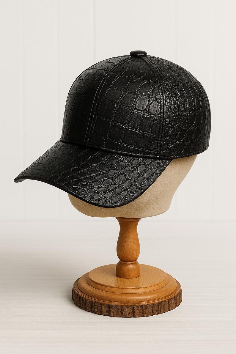 May include: Black baseball cap with a textured, crocodile-like pattern. The cap is displayed on a wooden hat stand with a round base. The hat has a curved brim and a button on top.