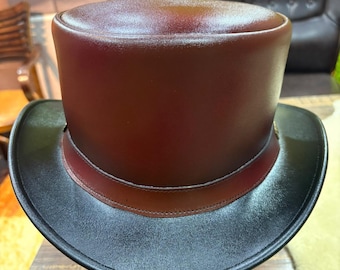 May include: A classic top hat with a dark burgundy crown and a black brim. The hat features a brown band around the base of the crown. The hat is displayed on a wooden hat stand.