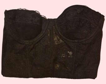 May include: A black lace bustier with a sweetheart neckline. The bustier has a structured design with molded cups and a scalloped trim along the top edge. The fabric appears to be a delicate, floral lace.