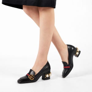 Peut inclure: Mocassins à talons blocs en cuir noir ornés d'un logo GG entrelacé doré, d'une bande web bleue et rouge sur le dessus, et d'un talon bloc décoré de perles synthétiques blanches et de petits clous dorés sur le côté extérieur du talon.