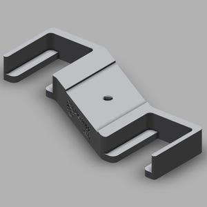 May include: A grey, 3D-rendered object with a rectangular central body and two U-shaped arms extending from either side. A small hole is visible in the centre. The object appears to be made of metal.