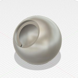 May include: A metallic silver sphere with a circular cut-out. The sphere has a smooth, reflective surface and casts a shadow on a grid background. The cut-out reveals an interior cavity.