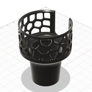 Puede incluir: Un portavasos negro con un diseño geométrico de panal en la parte superior. El soporte tiene una base cilíndrica y una parte superior curva y abierta, diseñada para sostener un recipiente para bebidas. El diseño es moderno y minimalista.