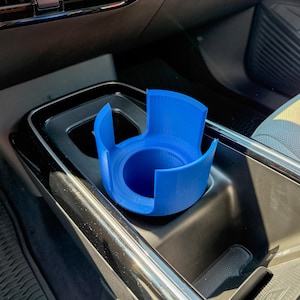 Puede incluir: Un portavasos azul brillante para coche, dise&ntilde;ado para la consola central de un veh&iacute;culo. El portavasos tiene una base circular y un dise&ntilde;o abierto con soportes curvos. El art&iacute;culo est&aacute; hecho de un material s&oacute;lido, posiblemente impreso en 3D.