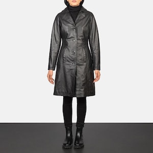 May include: A black leather coat with a notched collar and button closure. The coat has a knee-length hem and long sleeves. The person is wearing black pants and boots. The coat is a classic style.