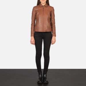 May include: A full-length shot of a person wearing a brown leather jacket and black pants. The jacket has a collar and a zipper closure. The pants are fitted. The person is wearing black boots.