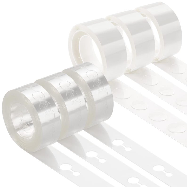 May include: Six rolls of clear adhesive tape arranged in two rows. Each roll features a series of circular, pre-cut adhesive tabs attached to a continuous backing strip. The tape is transparent, and the circular tabs are clearly visible on the rolls.