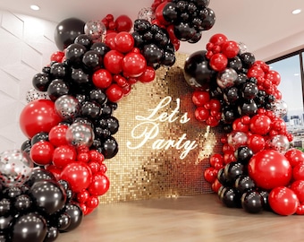 May include: A festive party backdrop featuring a gold sequin wall with the words "Let's Party" in white script. The arch is decorated with clusters of red, black, and silver balloons, creating a celebratory atmosphere.