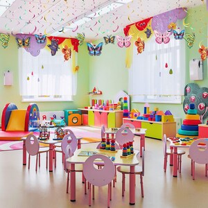 May include: A brightly colored playroom featuring multiple small tables and chairs, a yellow slide, colorful storage cabinets, various building blocks, stacking rings, and hanging butterfly decorations suspended from the ceiling.