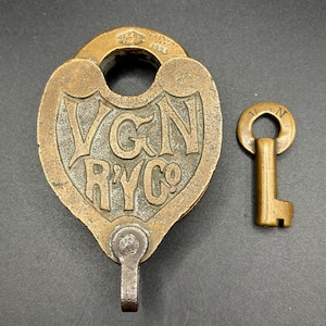 Puede incluir: Antiguo candado de latón con su llave. El candado tiene el texto "VGN RYC Co" y el año "1926" grabado. La llave es pequeña y tiene la letra "N".