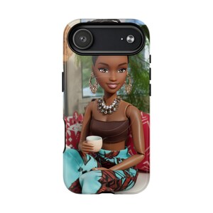 May include: A phone case featuring a doll with brown skin, wearing a brown top, patterned pants, and gold jewelry. The doll is holding a small white cup. The background shows a blurred outdoor scene.