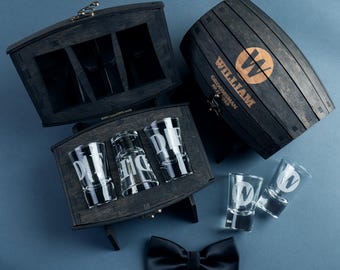 May include: A wooden barrel and boxes with shot glasses and a black bow tie. The barrel and boxes are dark stained wood. The shot glasses have the letter "W" etched on them. The barrel has the name "William" printed on it.