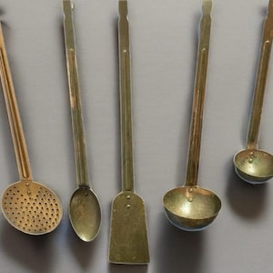 May include: Five vintage kitchen utensils are displayed against a gray background. The collection includes a slotted spoon, a solid spoon, a spatula, a ladle, and a small round scoop. Each utensil has a long handle and a metal head.