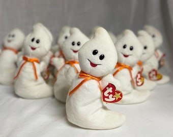 May include: A collection of white plush ghost toys with black button eyes, red smiling mouths, and orange ribbon bows. Each ghost has a red heart-shaped tag. The toys are a popular collectible item.