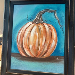 May include: An orange pumpkin painting in a black frame. The pumpkin is painted with orange and white brushstrokes, with a gray stem against a blue background. The painting is signed in the bottom right corner.