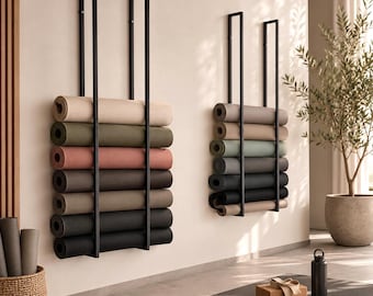 May include: Two wall-mounted black metal racks hold multiple rolled yoga mats in various neutral colors including beige, olive green, dusty rose, gray, and black. The racks feature vertical bars that secure the mats in a stacked arrangement.
