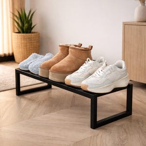 Puede incluir: Un zapatero de metal negro con varios pares de zapatos. Incluye zapatillas azules claras, botas de plataforma color canela y zapatillas deportivas blancas. El zapatero está sobre un suelo de madera clara.