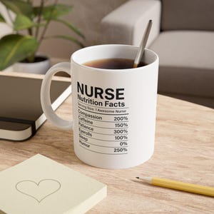 May include: White ceramic mug with the text "NURSE Nutrition Facts" and a list of humorous nutritional values. The mug contains a dark liquid and a silver spoon. A yellow pencil and a notepad are in the foreground.
