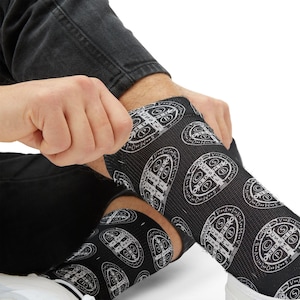 May include: Black socks with a repeating white graphic pattern. The socks are pulled up on the legs. The graphic pattern is a circular design with text and a cross.