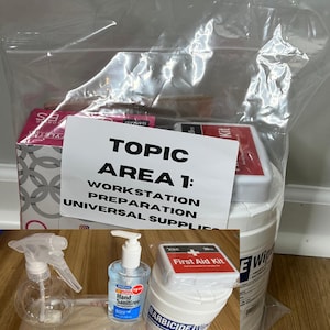 May include: A clear plastic bag containing various workstation preparation and universal supplies. Items include a spray bottle, hand sanitizer, a first aid kit, gloves, and Barbicide wipes. The bag has a white label with the text "TOPIC AREA 1: WORKSTATION PREPARATION UNIVERSAL SUPPLIES."
