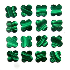 May include: Sixteen green malachite clover-shaped gemstones. Each stone features a unique pattern of dark and light green bands, resembling natural wood grain. The gemstones are arranged on a white background.