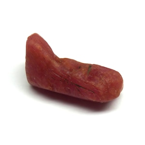Può includere: Una pietra di colore rosso-arancio, di forma irregolare e dall'aspetto liscio e lucido. La pietra ha una forma leggermente curva e sembra essere un esemplare naturale non raffinato. La superficie mostra sottili variazioni di colore e consistenza, con venature più scure.