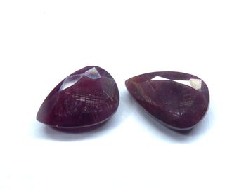 Könnte beinhalten: Zwei facettierte, birnenförmige Edelsteine in tiefroter Farbe. Die Edelsteine haben eine polierte Oberfläche mit sichtbaren inneren Strukturen und einer hellen, reflektierenden Facette. Die Edelsteine sind vor weißem Hintergrund platziert.