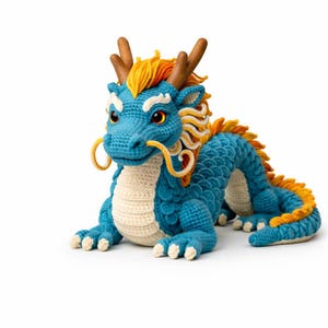 May include: A handcrafted, blue crochet dragon with yellow and orange accents. The dragon features detailed scales, horns, and a cream-colored belly. Its eyes are red, and it has yellow whiskers. The dragon is lying down, showcasing its intricate design.