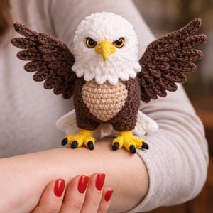 Puede incluir: Un águila de ganchillo hecha a mano con cabeza blanca, alas marrones y pecho beige. El águila tiene patas amarillas con garras negras y un pico amarillo. Las alas están extendidas y el águila parece estar posada.