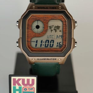 May include: A digital Casio watch with a brown wood-grain face and a green leather strap. The watch displays the time as 11:00 and the date as 3-29. The watch has the text "WORLD TIME" and "ILLUMINATOR" on the face.