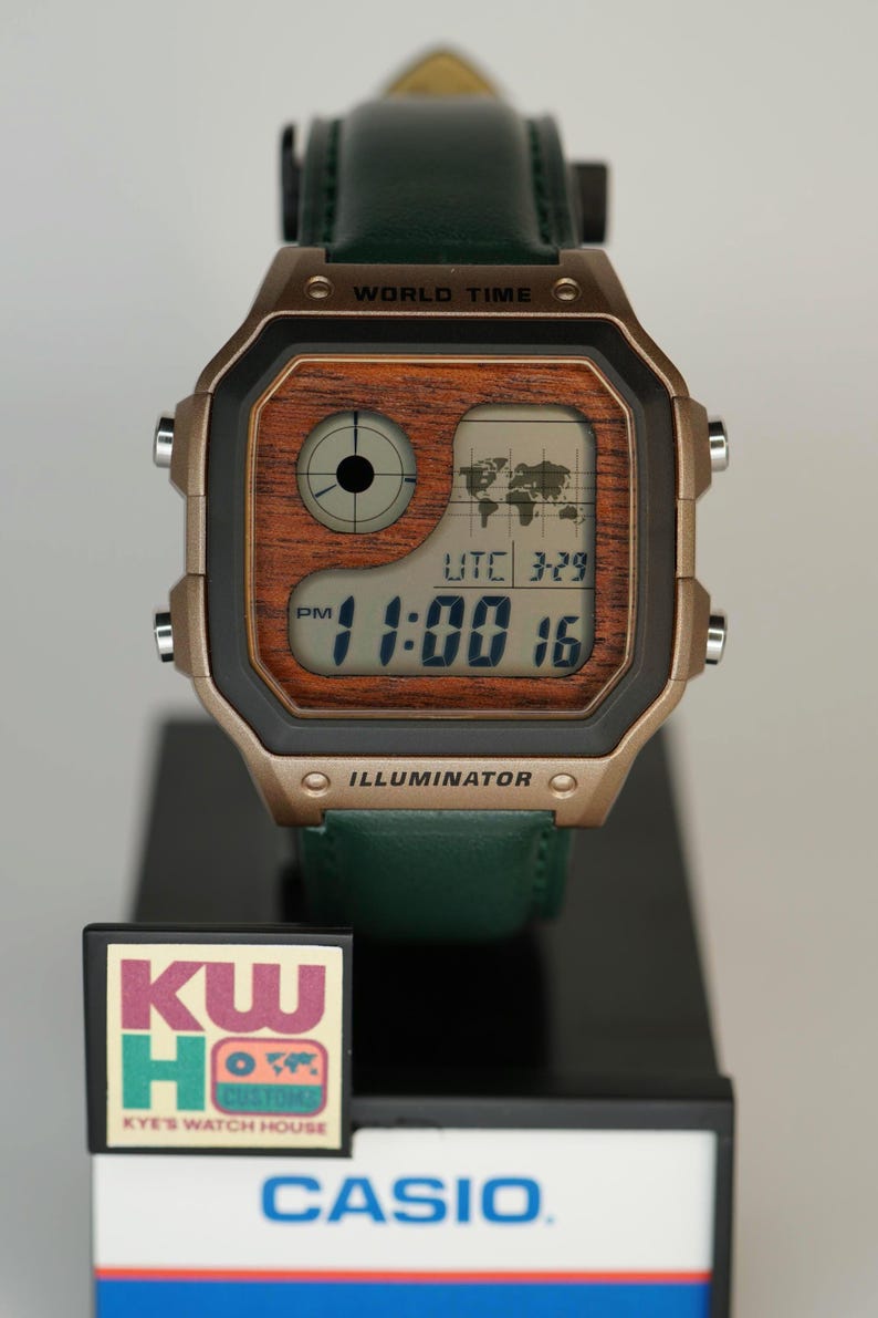 May include: A digital Casio watch with a brown wood-grain face and a green leather strap. The watch displays the time as 11:00 and the date as 3-29. The watch has the text "WORLD TIME" and "ILLUMINATOR" on the face.