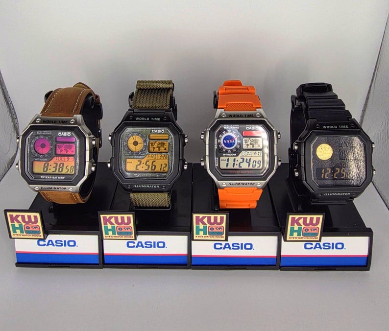 Puede incluir: Cuatro relojes digitales Casio en exhibici&oacute;n. Los relojes tienen varias correas de colores, incluyendo cuero marr&oacute;n, verde oliva, naranja y negro. Cada reloj muestra la hora y tiene una pantalla digital. La pantalla tambi&eacute;n muestra la palabra "ILLUMINATOR".