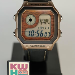 May include: A digital Casio watch with a brown wood-grain face and gold-tone case. The watch displays the time, 10:56:07, and features a world map graphic. The black leather band is stitched. The watch is on a black display stand.