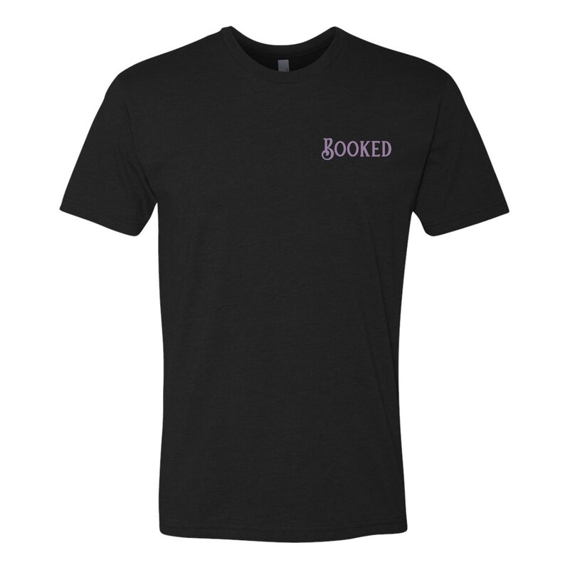 Puede incluir: Camiseta negra con la palabra "BOOKED" en escritura lila claro en el pecho. La camiseta tiene mangas cortas y cuello redondo. La tela parece ser un material suave y c&oacute;modo.