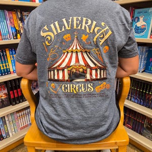 Puede incluir: Camiseta gris con un diseño de circo. El diseño presenta una carpa de circo con rayas rojas y blancas, el texto "SILVERICH CIRCUS" y la cita "It's okay to love your darkness and still love yourself. It doesn't make you a bad person. It makes you a whole lot."