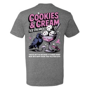 Puede incluir: Camiseta gris con un dise&ntilde;o gr&aacute;fico que presenta un cuervo, un helado y una calavera. El texto dice "COOKIES & CREAM ICE CREAM" en rosa y blanco. Debajo del gr&aacute;fico est&aacute; el texto: "TASTES BETTER BECAUSE IT'S MADE RIGHT MADE WITH MORE CREAM THAN THE OTHER GUYS."