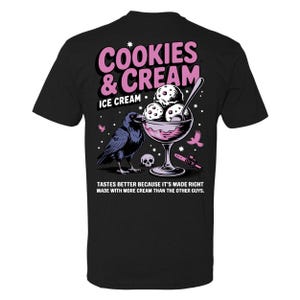 Puede incluir: Camiseta negra con un dise&ntilde;o gr&aacute;fico que presenta un cuervo, un helado y el texto "COOKIES & CREAM ICE CREAM". El dise&ntilde;o incluye una calavera y una motosierra. El texto de abajo dice: "TASTES BETTER BECAUSE IT'S MADE RIGHT MADE WITH MORE CREAM THAN THE OTHER GUYS."